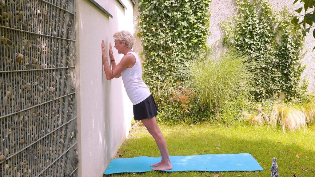 Colette, debout face à un mur, plie les coudes et approche le buste du mur, le corps gainé